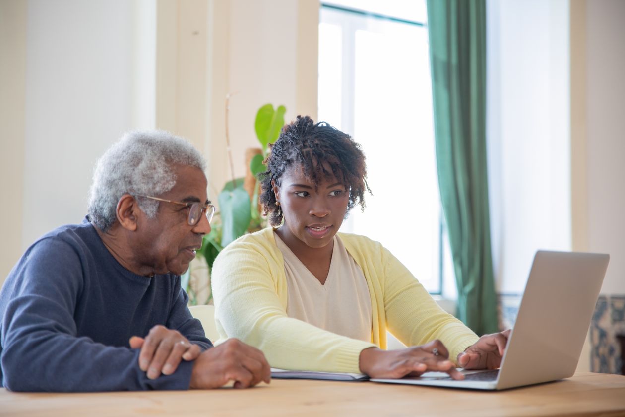 A younger woman helping an older man with a laptop at home.